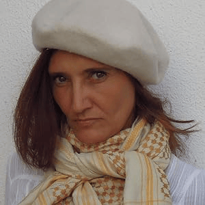 A woman wearing a white beret and a patterned scarf, with shoulder-length brown hair and a serious expression.